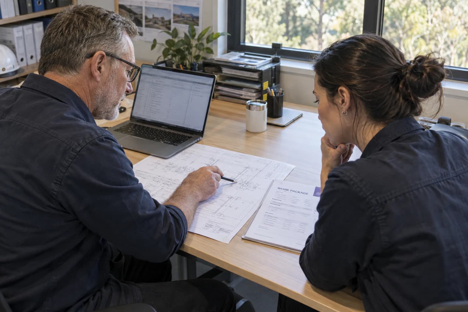 Two people go through a drawing and a work package at a desk.