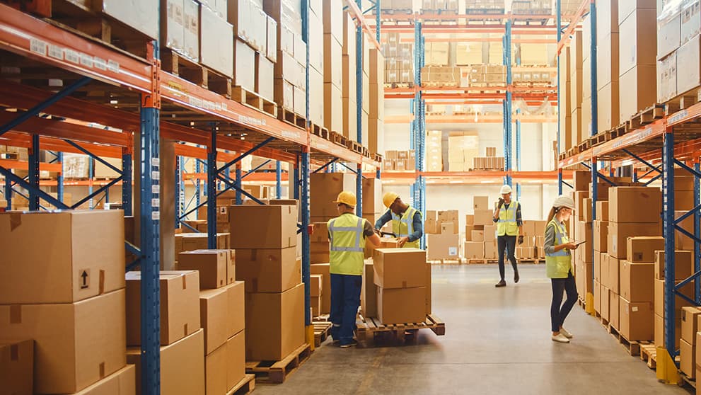 A warehouse team moving and checking cartons in storage aisles